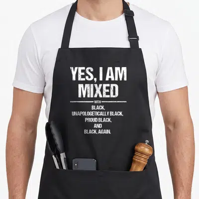 Proud african apron - White stacked text yes i am mixed with black unapologetically proud black again — shown on a black cotton canvas apron against a white background