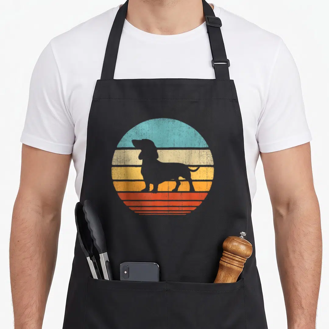 60s dachshund apron - Grey dachshund silhouette over blue yellow orange red striped semi-circle — shown on a black cotton canvas apron against a white background