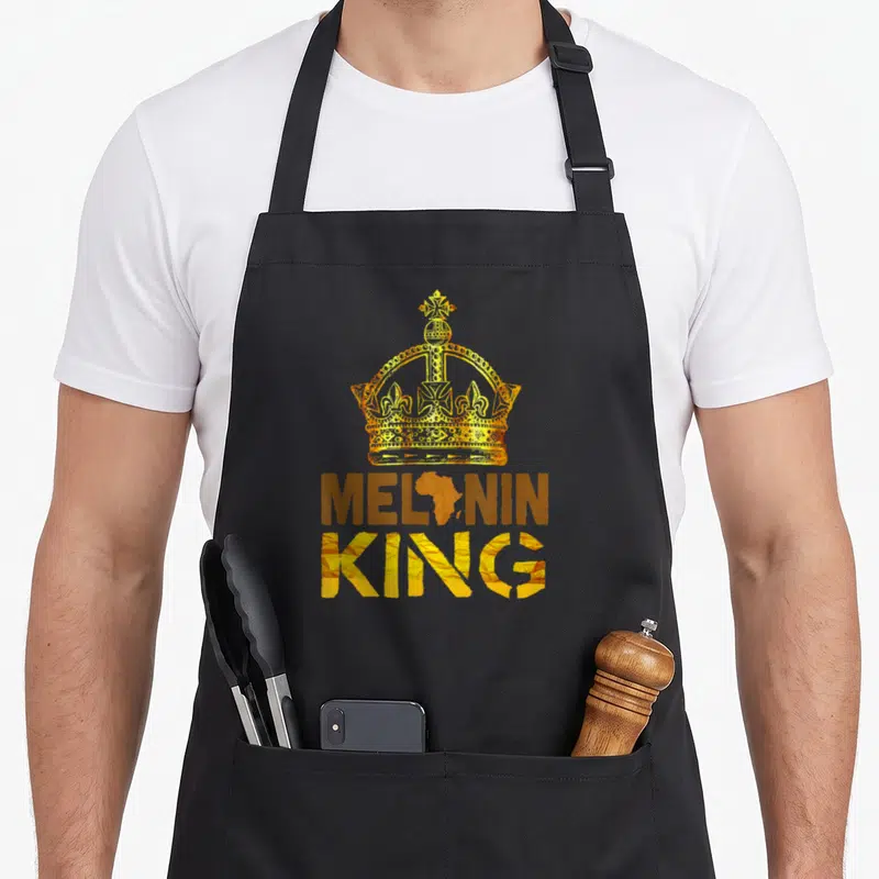 Melanin king apron - Gold crown above MELONIN KING with Africa map replacing O, brown and gold retro design — shown on a black cotton canvas apron against a white background