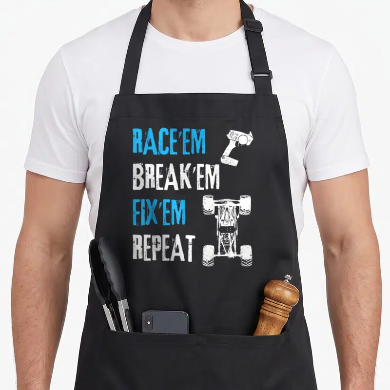 Remote car apron - Distressed blue and white text RACE'EM BREAK'EM FIX'EM REPEAT with RC car and controller silhouettes — shown on a black cotton canvas apron against a white background