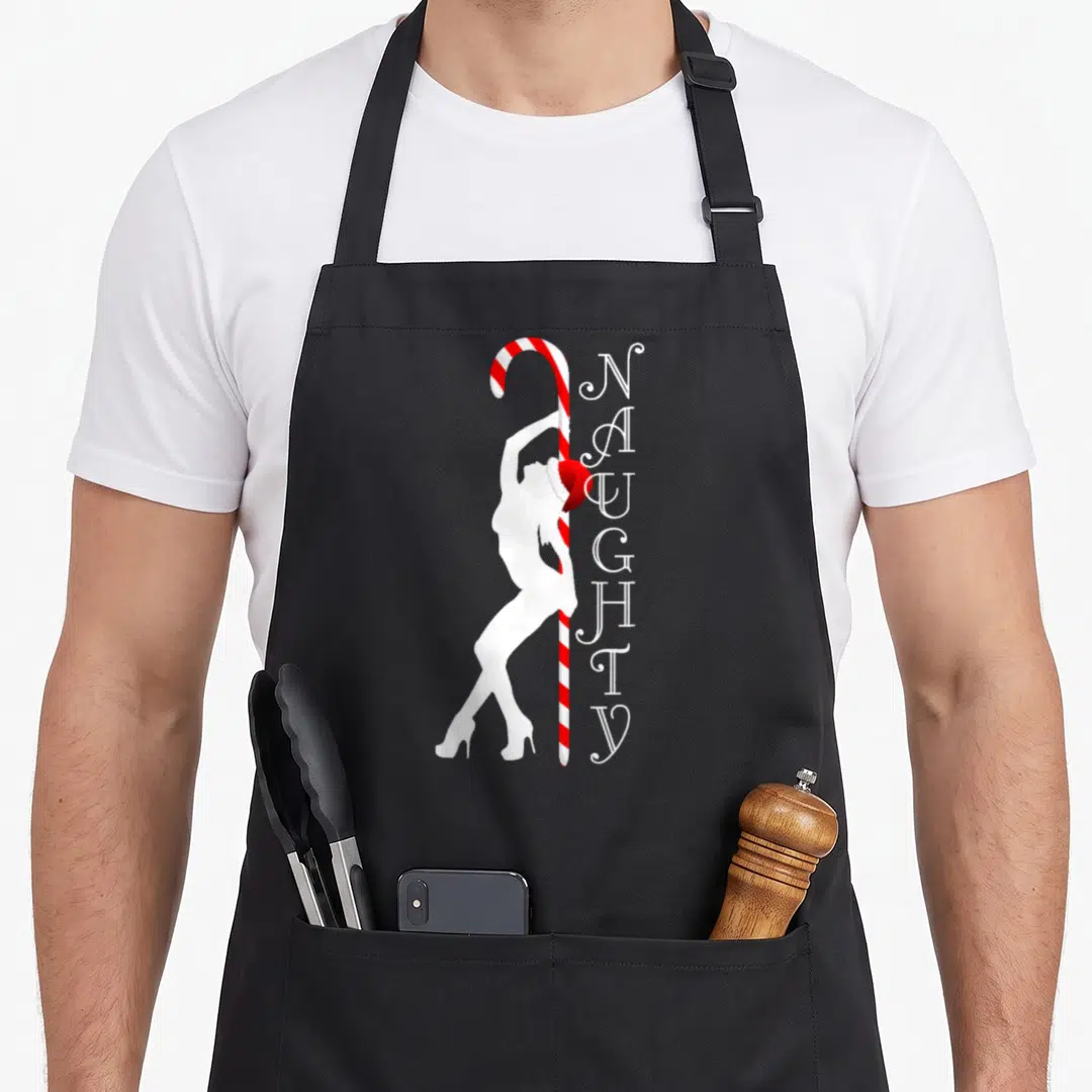 Naughty ugly sweater apron - White woman silhouette leaning on red white striped candy cane with vertical NAUGHTY text — shown on a black cotton canvas apron against a white background