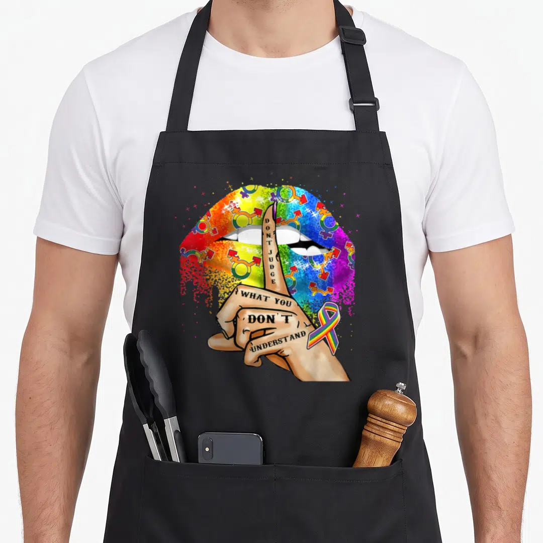 Judge pride apron - Cartoon hand shushing over rainbow lips with gender symbols and wrist ribbon — shown on a black cotton canvas apron against a white background