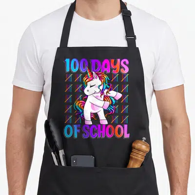 Smarter unicorn apron - Cartoon unicorn dabbing with 100 DAYS OF SCHOOL text and rainbow tally marks — shown on a black cotton canvas apron against a white background