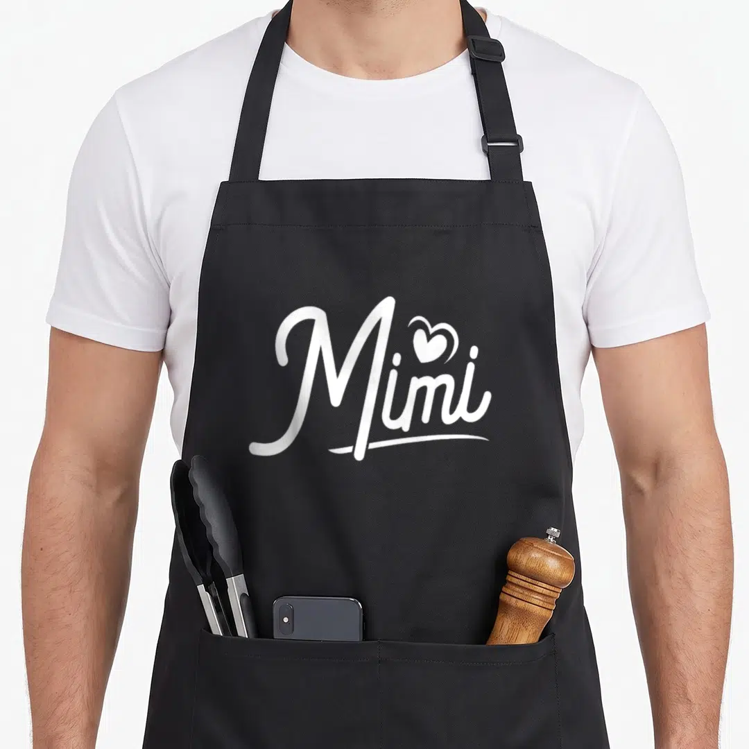 Grandchildren mimi apron - White script Mimi text with heart replacing dot and underline swoosh — shown on a black cotton canvas apron against a white background
