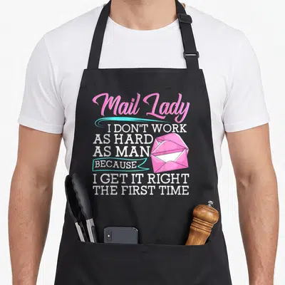 Hard postal aprons - Stacked white text reading Mail Lady with pink envelope and cyan ribbon banner — shown on a black cotton canvas apron against a white background