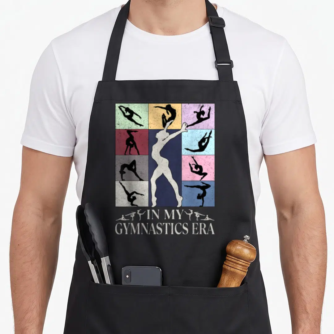 Gymnast birthday apron - In My Gymnastics Era text below white silhouette on colorful grid of black gymnast poses — shown on a black cotton canvas apron against a white background