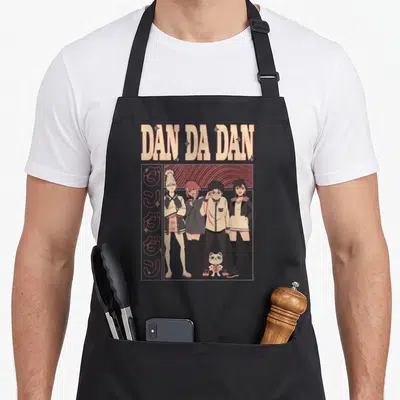 Dan character aprons - Four cartoon characters and cat statue under DAN DA DAN text with red stripes and vertical script — shown on a black cotton canvas apron against a white background