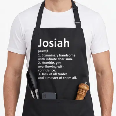 Josiah father day aprons - White typography listing three definitions for Josiah including handsome and master of all — shown on a black cotton canvas apron against a white background