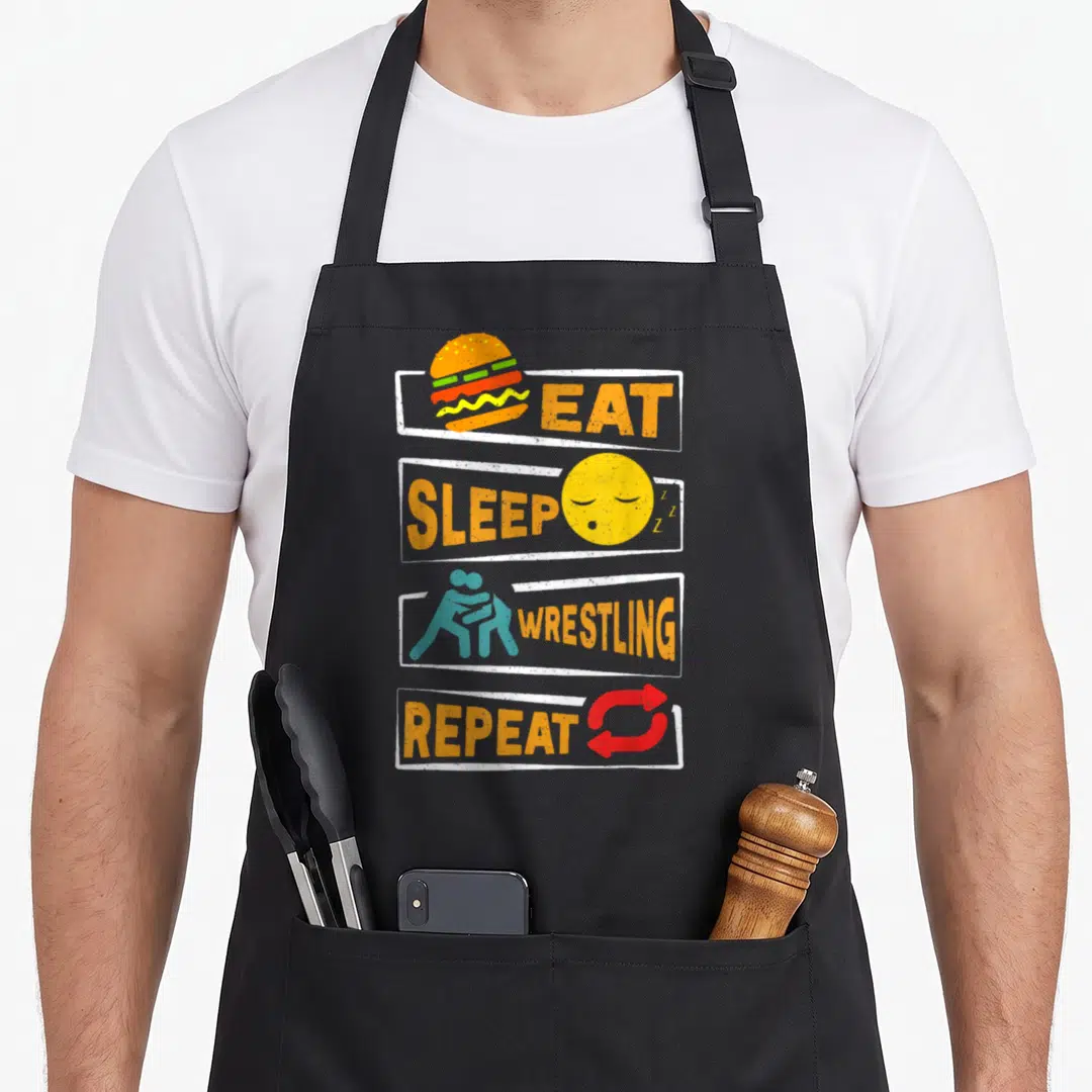 Repeat wrestling apron - Four stacked frames with Eat Sleep Wrestling Repeat text and cartoon icons in orange, yellow — shown on a black cotton canvas apron against a white background