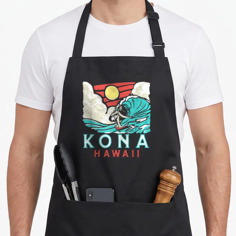 Kona 80s apron - Retro surfer on teal wave with yellow sun and Kona Hawaii text — shown on a black cotton canvas apron against a white background