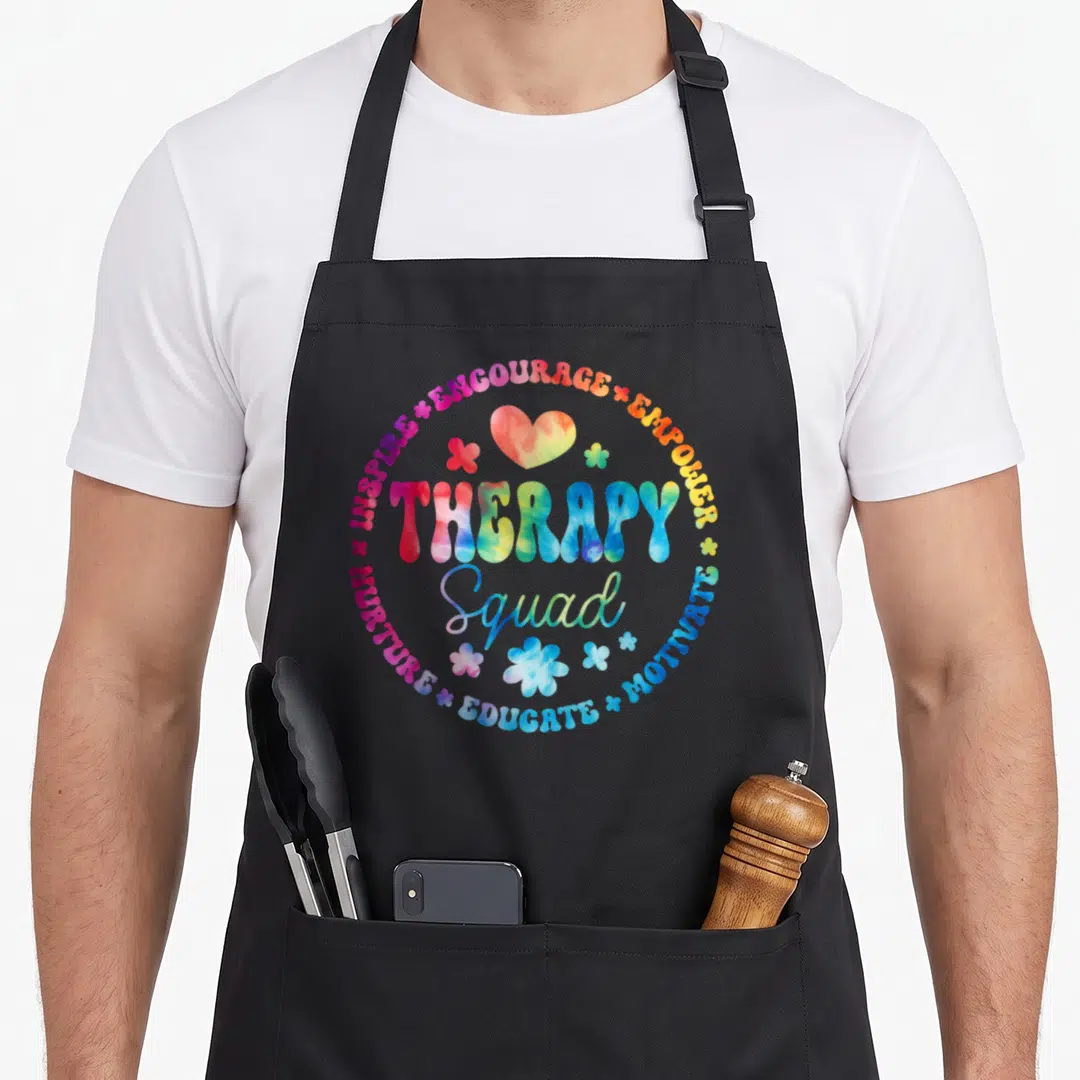 Week my therapy apron - Tie-dye text circle with inspire encourage empower motivate educate nurture therapy squad words — shown on a black cotton canvas apron against a white background