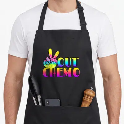 Peace cancer apron - Tie-dye hand peace sign next to OUT CHEMO text — shown on a black cotton canvas apron against a white background