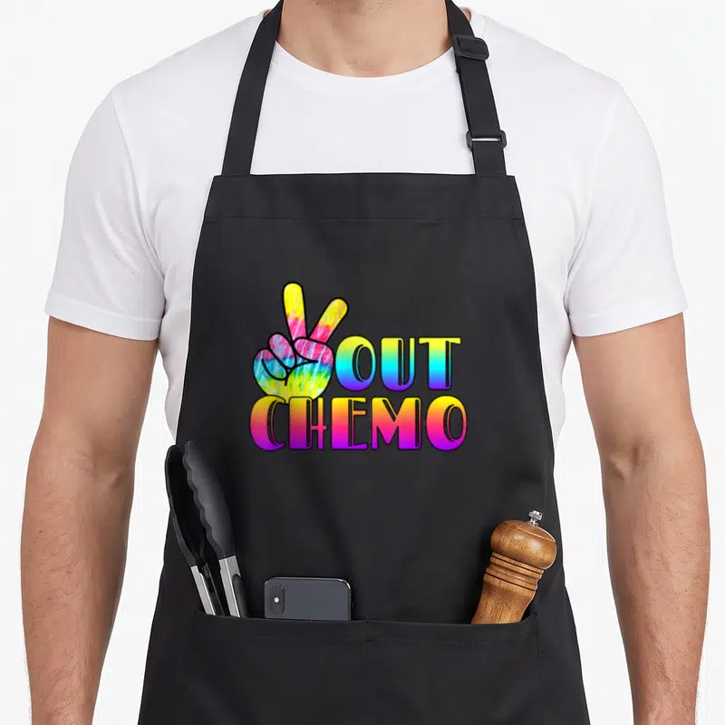 Peace cancer apron - Tie-dye hand peace sign next to OUT CHEMO text — shown on a black cotton canvas apron against a white background