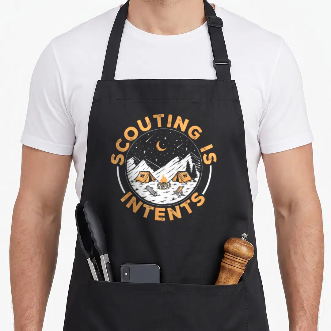 Scouting camping apron - Circular campsite with orange tents and fire, surrounded by arched text SCOUTING IS INTENTS — shown on a black cotton canvas apron against a white background