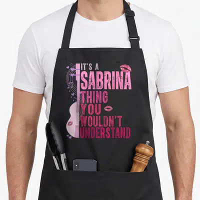 Sabrina its birthday apron - Pink guitar graphic with stacked text IT'S A SABRINA THING YOU WOULDN'T UNDERSTAND — shown on a black cotton canvas apron against a white background