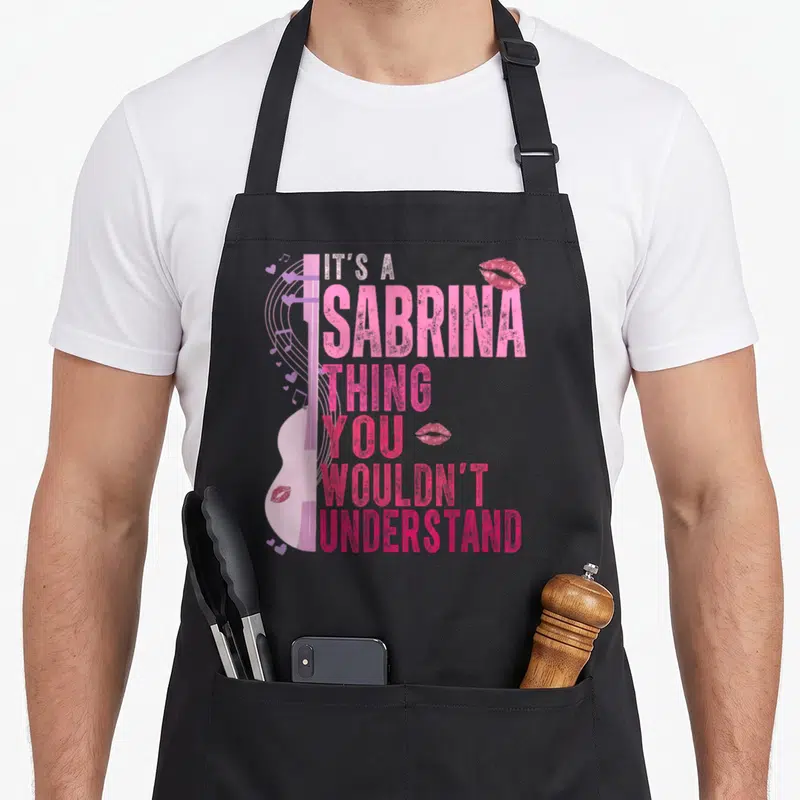 Sabrina its birthday apron - Pink guitar graphic with stacked text IT'S A SABRINA THING YOU WOULDN'T UNDERSTAND — shown on a black cotton canvas apron against a white background