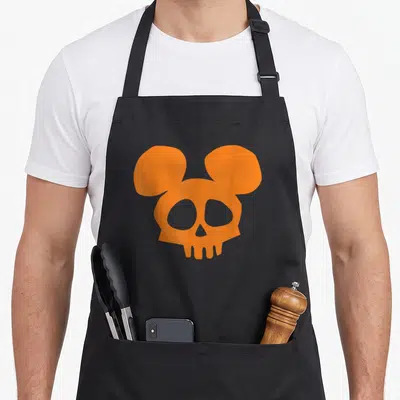 Skull halloween apron - Minimalist orange skull silhouette with large round mouse ears and cutout teeth — shown on a black cotton canvas apron against a white background