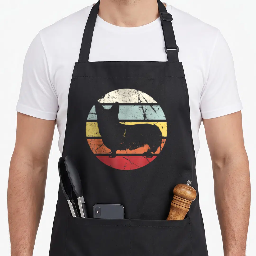 Distressed corgi aprons - Grey dog silhouette over distressed circle of cream blue yellow orange and red horizontal — shown on a black cotton canvas apron against a white background