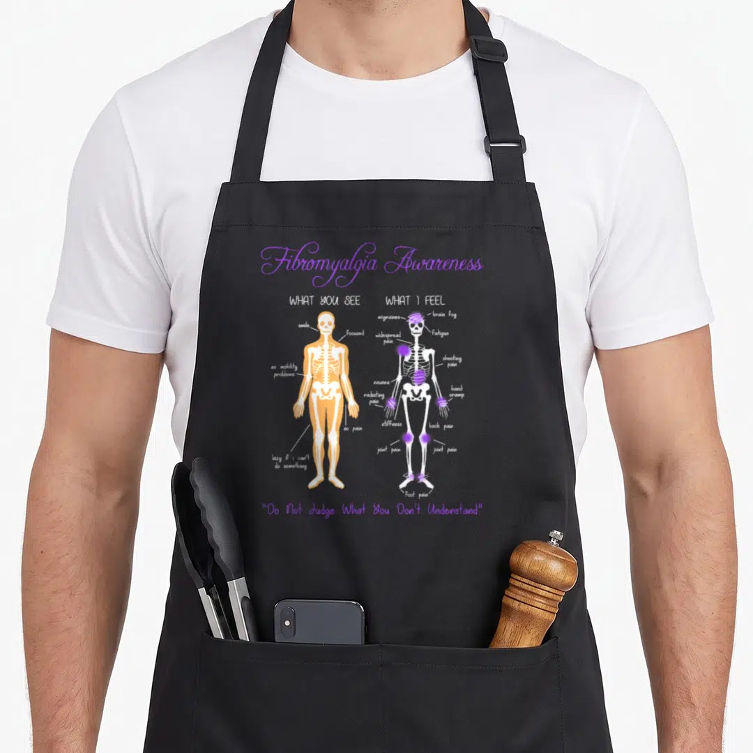 See skeleton apron - Two skeletons comparing visible health versus fibromyalgia pain symptoms with purple markers — shown on a black cotton canvas apron against a white background