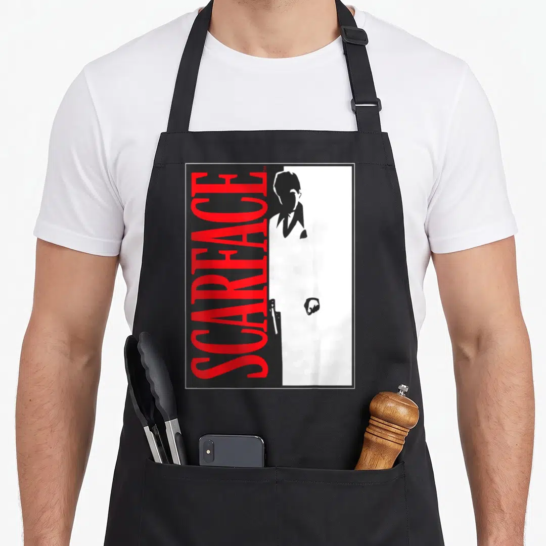 Scarface hypebeast apron - Vertical red SCARFACE text next to a white suited man silhouette holding a gun on black — shown on a black cotton canvas apron against a white background