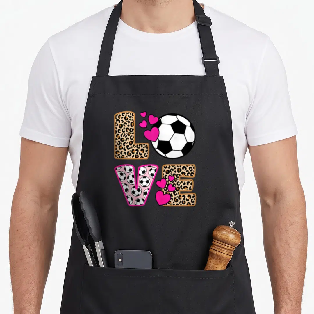 Soccer leopard apron - LOVE text with soccer ball O, pink hearts, and tan leopard print letters — shown on a black cotton canvas apron against a white background