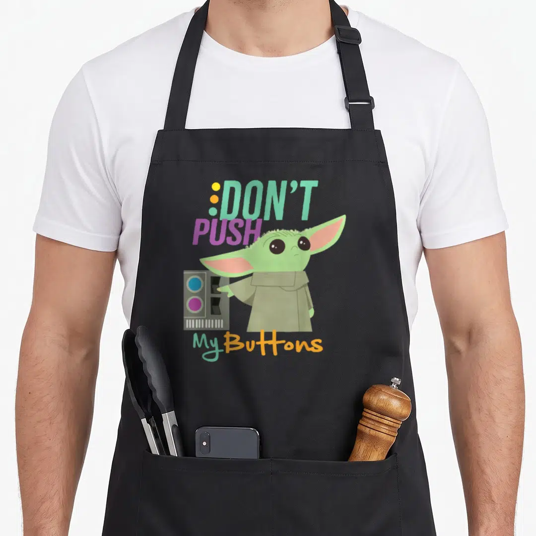 Push wars new apron - Cartoon Grogu reaching for grey panel with DON'T PUSH My Buttons text in green, pink, orange, grey — shown on a black cotton canvas apron against a white background