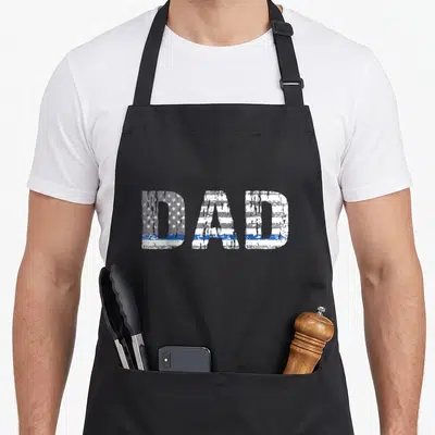 Supporter line apron - DAD text filled with distressed American flag and thin blue stripe in white, blue, grey — shown on a black cotton canvas apron against a white background