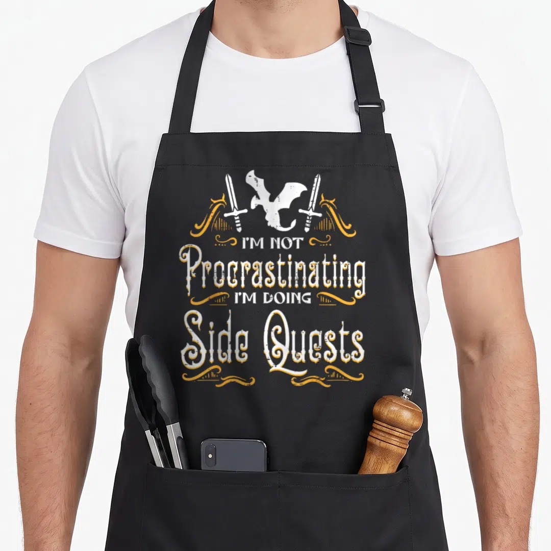 Rpg dungeon apron - Dragon and two swords above stacked text reading I'M NOT Procrastinating I'M DOING Side Quests — shown on a black cotton canvas apron against a white background