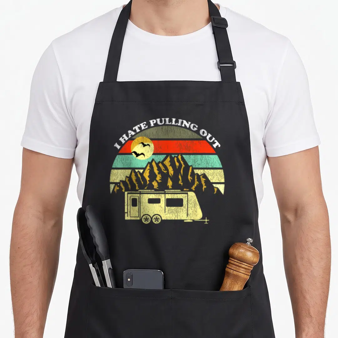 Pulling camping apron - Retro camper trailer with striped sun and mountains under arched text — shown on a black cotton canvas apron against a white background