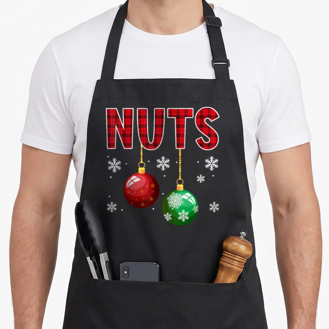 Nut couples christmas aprons - Red plaid NUTS text with hanging red and green ornaments and white snowflakes — shown on a black cotton canvas apron against a white background