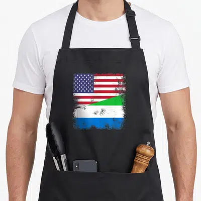 Flag sierra apron - Distressed square graphic merging US stars stripes and Sierra Leone green white blue bands split — shown on a black cotton canvas apron against a white background