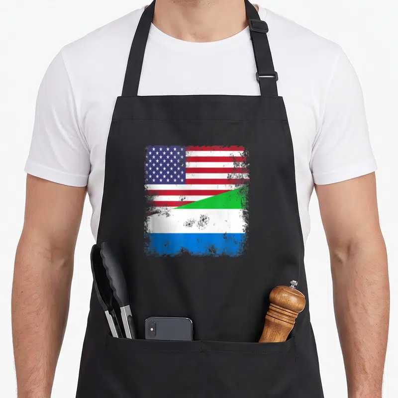 Flag sierra apron - Distressed square graphic merging US stars stripes and Sierra Leone green white blue bands split — shown on a black cotton canvas apron against a white background