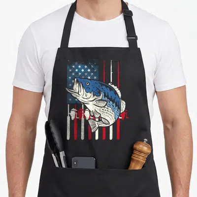 Bass fish american flag apron - Large bass fish over distressed flag with fishing rod stripes in blue red white — shown on a black cotton canvas apron against a white background