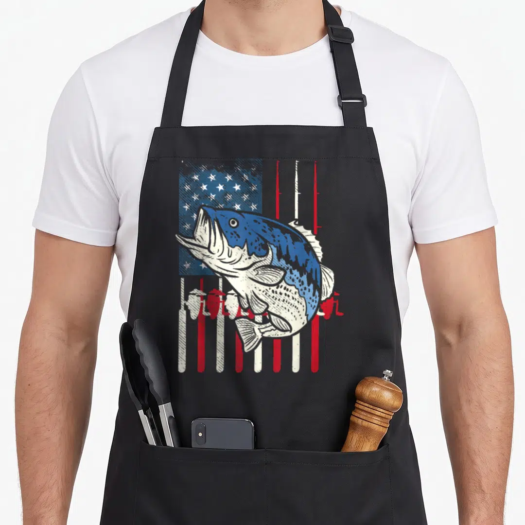 Bass fish american flag apron - Large bass fish over distressed flag with fishing rod stripes in blue red white — shown on a black cotton canvas apron against a white background