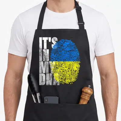 Dna ukrainian aprons - IT'S IN MY DNA text next to blue yellow distressed fingerprint — shown on a black cotton canvas apron against a white background
