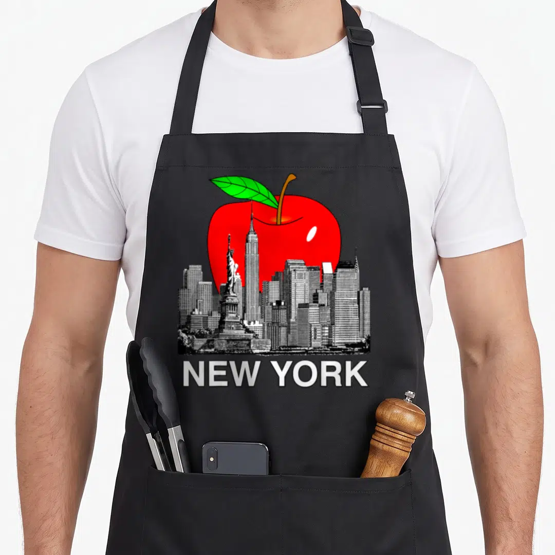 Apple new york apron - Red apple behind black and white NYC skyline with NEW YORK text below — shown on a black cotton canvas apron against a white background