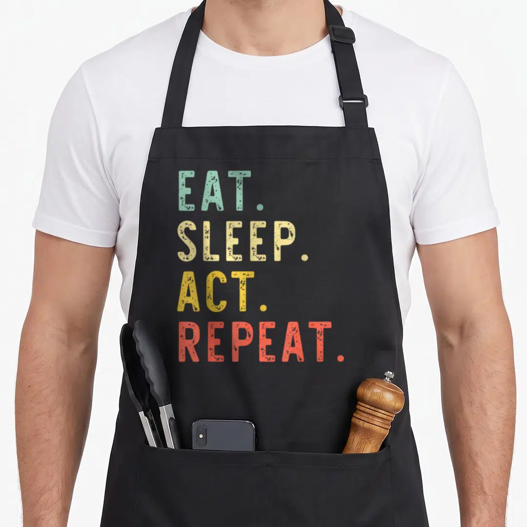 Eat acting apron - Stacked text EAT SLEEP ACT REPEAT in teal beige yellow and coral — shown on a black cotton canvas apron against a white background