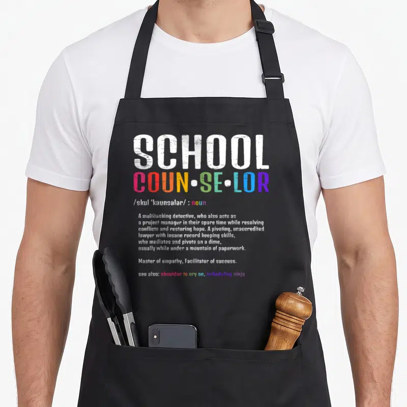 Cute school counselor apron - Dictionary style typography defining School Counselor in white and rainbow letters — shown on a black cotton canvas apron against a white background