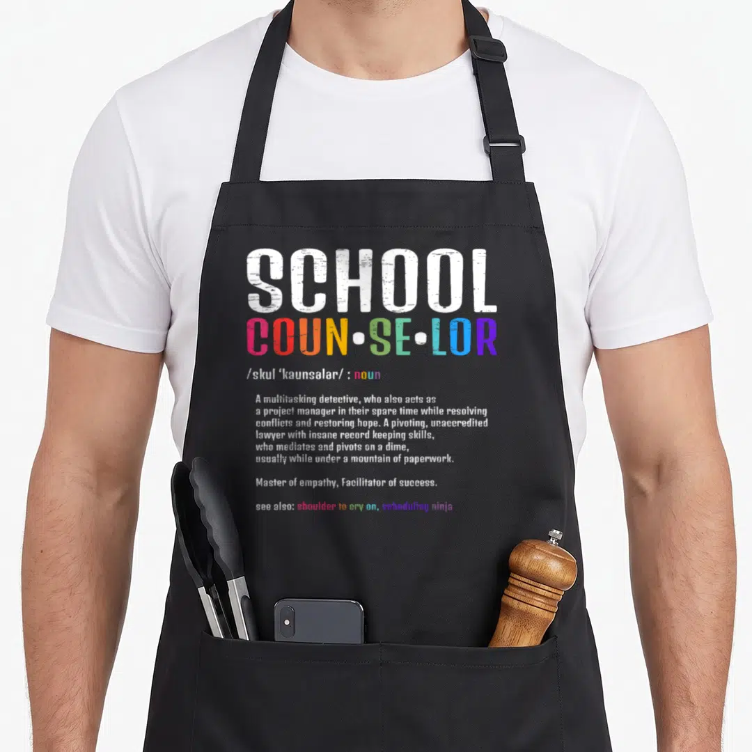 Cute school counselor apron - Dictionary style typography defining School Counselor in white and rainbow letters — shown on a black cotton canvas apron against a white background