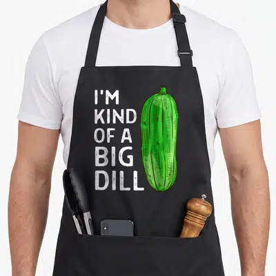 Kind joke apron - Stacked white text reading I'm Kind of a Big Dill next to a large green cartoon pickle — shown on a black cotton canvas apron against a white background