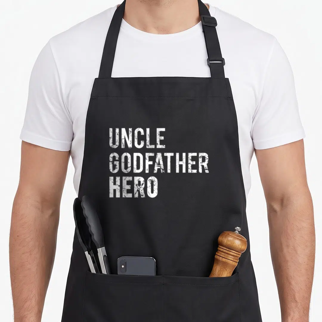 Godfather family aprons - White distressed text reading UNCLE GODFATHER HERO stacked in three lines — shown on a black cotton canvas apron against a white background