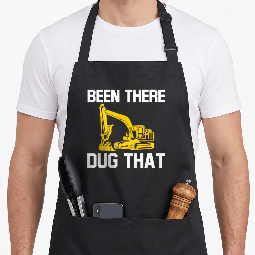 Dug heavy canvas aprons - Yellow excavator graphic between white BEEN THERE DUG THAT text — shown on a black cotton canvas apron against a white background
