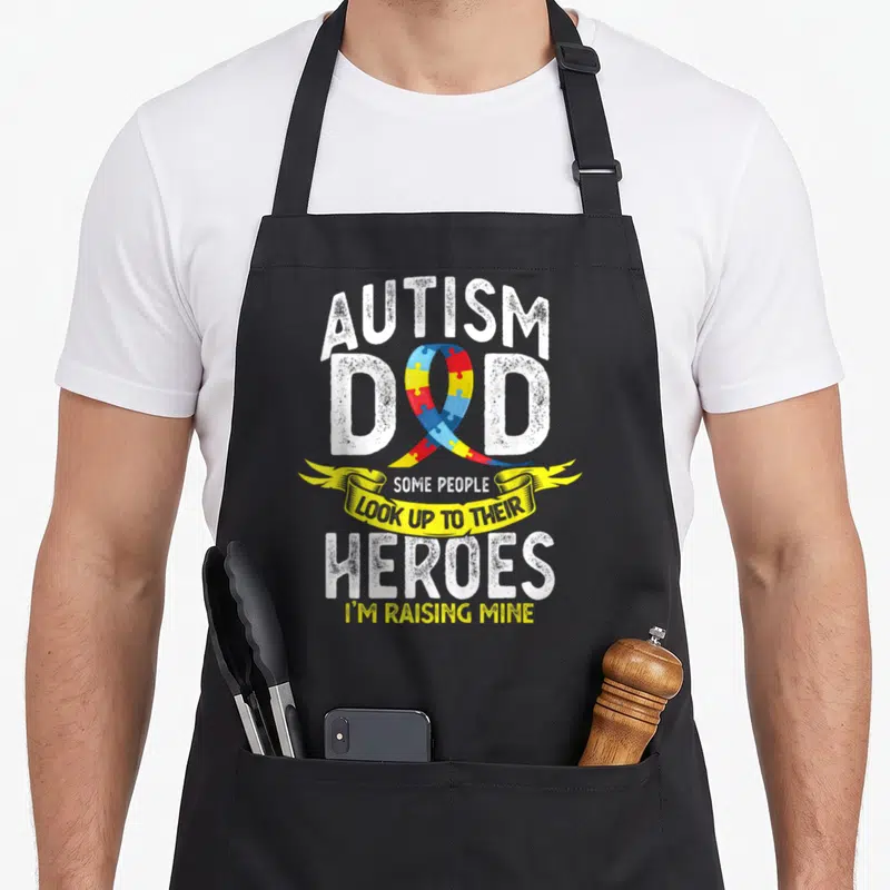 Their autism dad apron - Puzzle piece ribbon overlaps AUTISM DAD text with yellow banner reading Some People Look Up — shown on a black cotton canvas apron against a white background