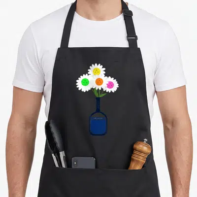 Pickleball pretty apron - Four daisies with colored centers in dark blue pickleball racket vase cartoon art — shown on a black cotton canvas apron against a white background
