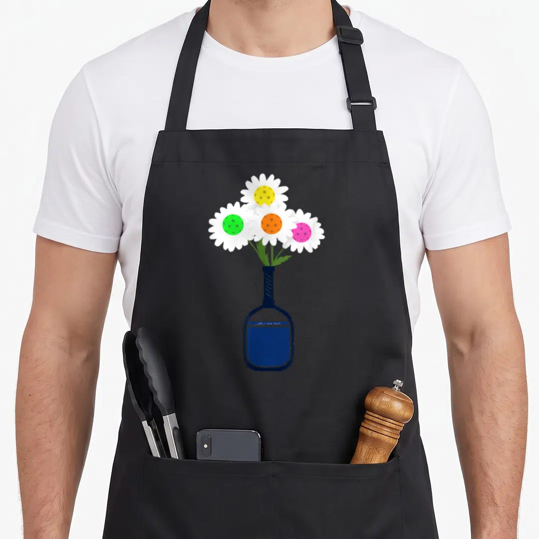 Pickleball pretty apron - Four daisies with colored centers in dark blue pickleball racket vase cartoon art — shown on a black cotton canvas apron against a white background