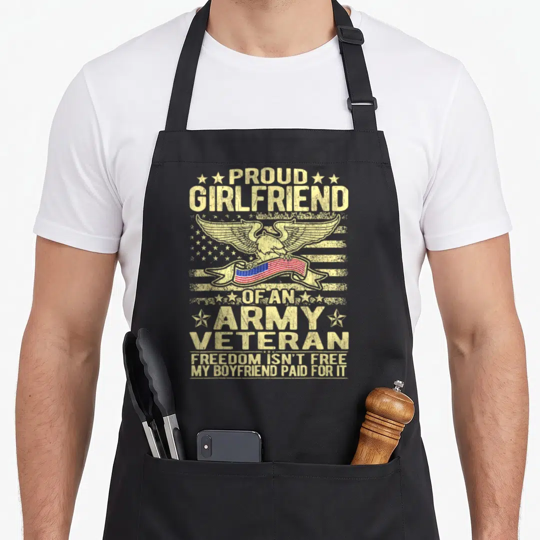 Freedom military apron - Distressed eagle holding red white blue flag ribbon surrounded by stacked text and stars — shown on a black cotton canvas apron against a white background