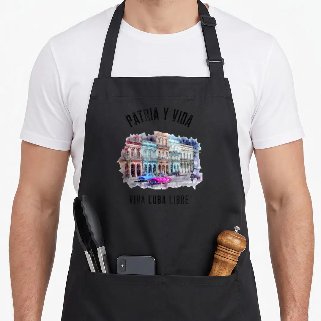 Dictadura cuba libre apron - PATRIA Y VIDA text over watercolor Havana buildings and pink blue cars — shown on a black cotton canvas apron against a white background