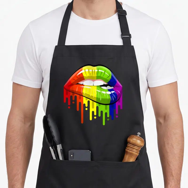 Lip rainbow apron - Rainbow lips with red orange yellow green blue purple paint dripping over white teeth — shown on a black cotton canvas apron against a white background