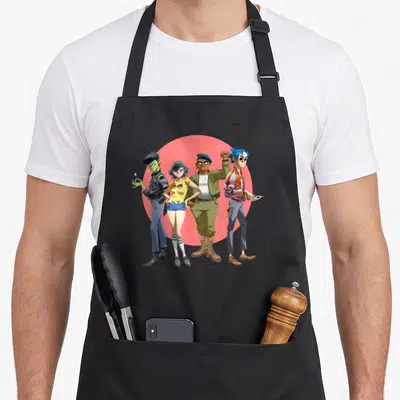 Gorillaz band apron - Four cartoon figures in front of red circle, wearing olive, blue, yellow, and red — shown on a black cotton canvas apron against a white background