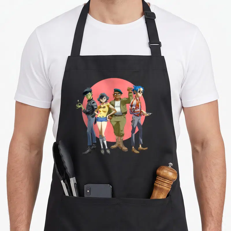 Gorillaz band apron - Four cartoon figures in front of red circle, wearing olive, blue, yellow, and red — shown on a black cotton canvas apron against a white background